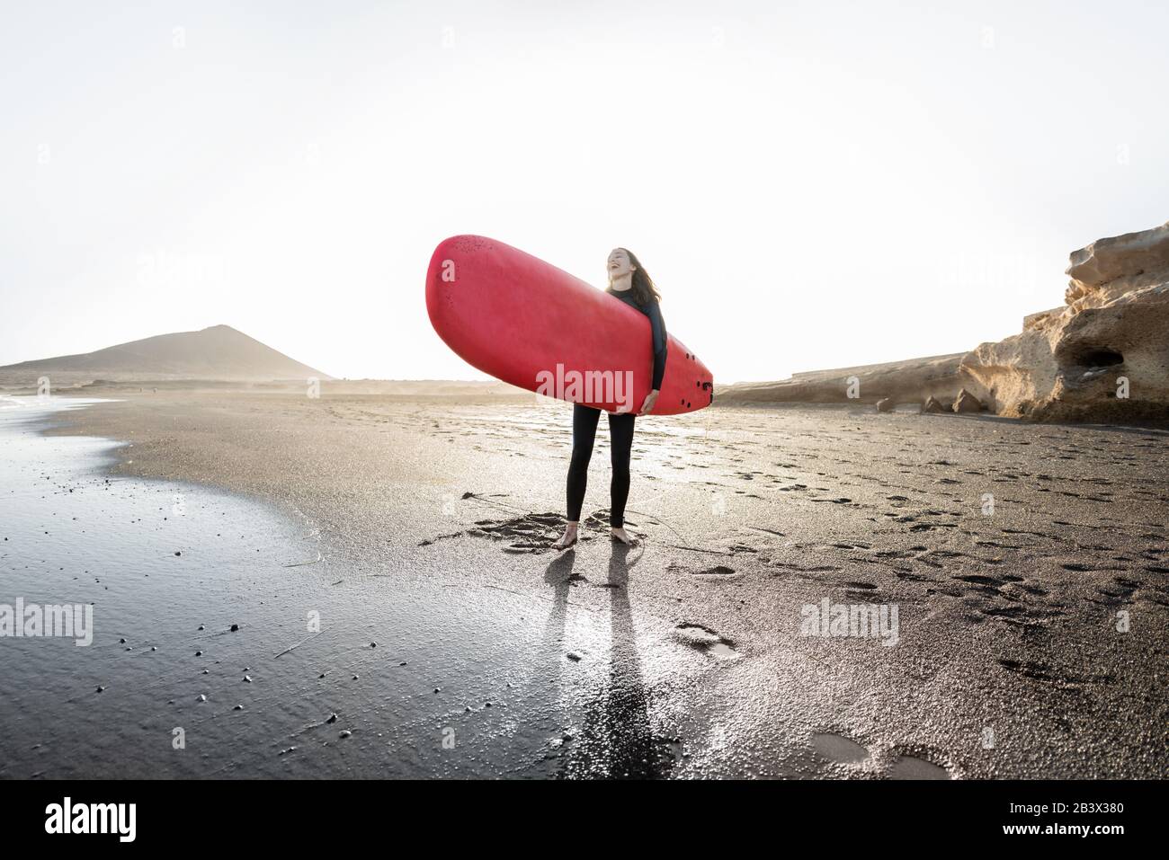 Young surfer in wetsuit running with surfboard to the sea. Summer activities and active