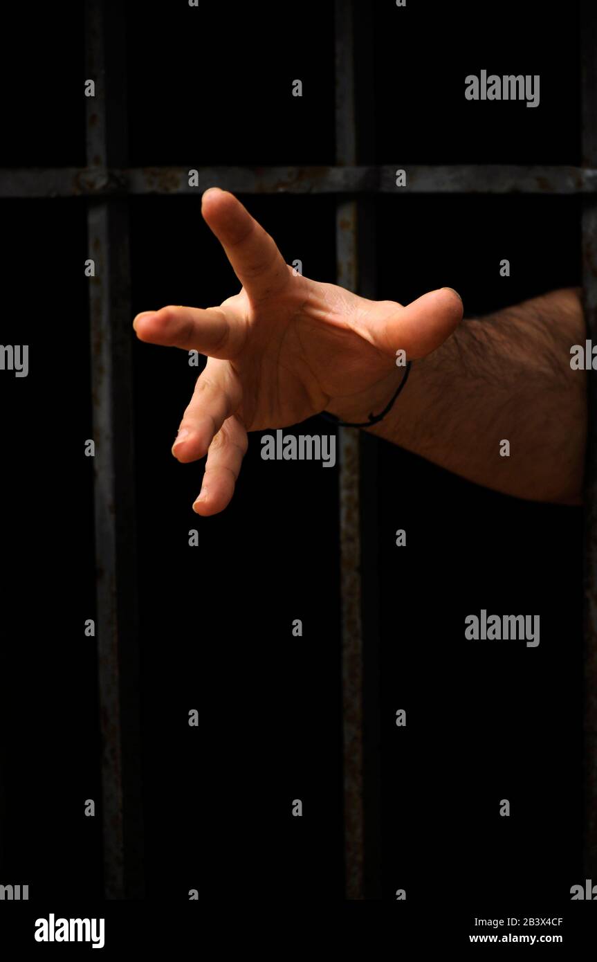 Man hand going out from a room of prison with bars/ Hands Through Prison Bars/ Abstract imagery for book covers/ feeling of confinement Stock Photo