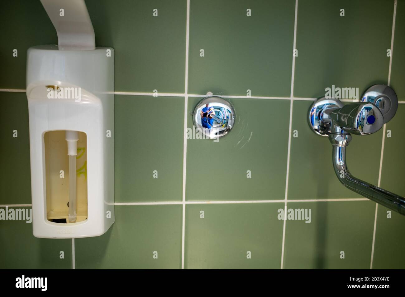 an empty disinfectant dispenser hangs on the wall next to a tap Stock ...