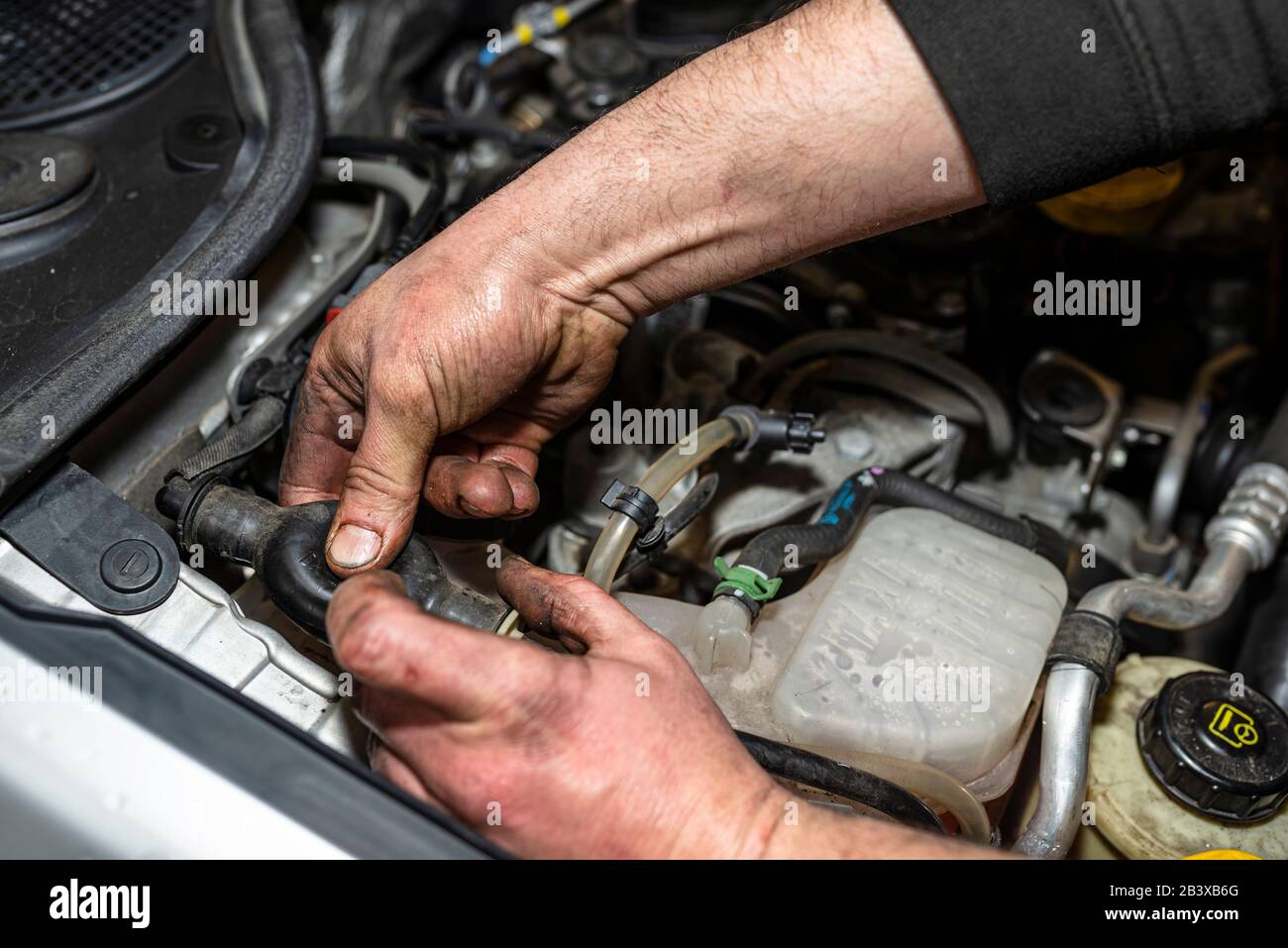 The mechanic bleeds the fuel system with a pump that is on the fuel line, after installing a new fuel filter, the man hands are visible. Stock Photo