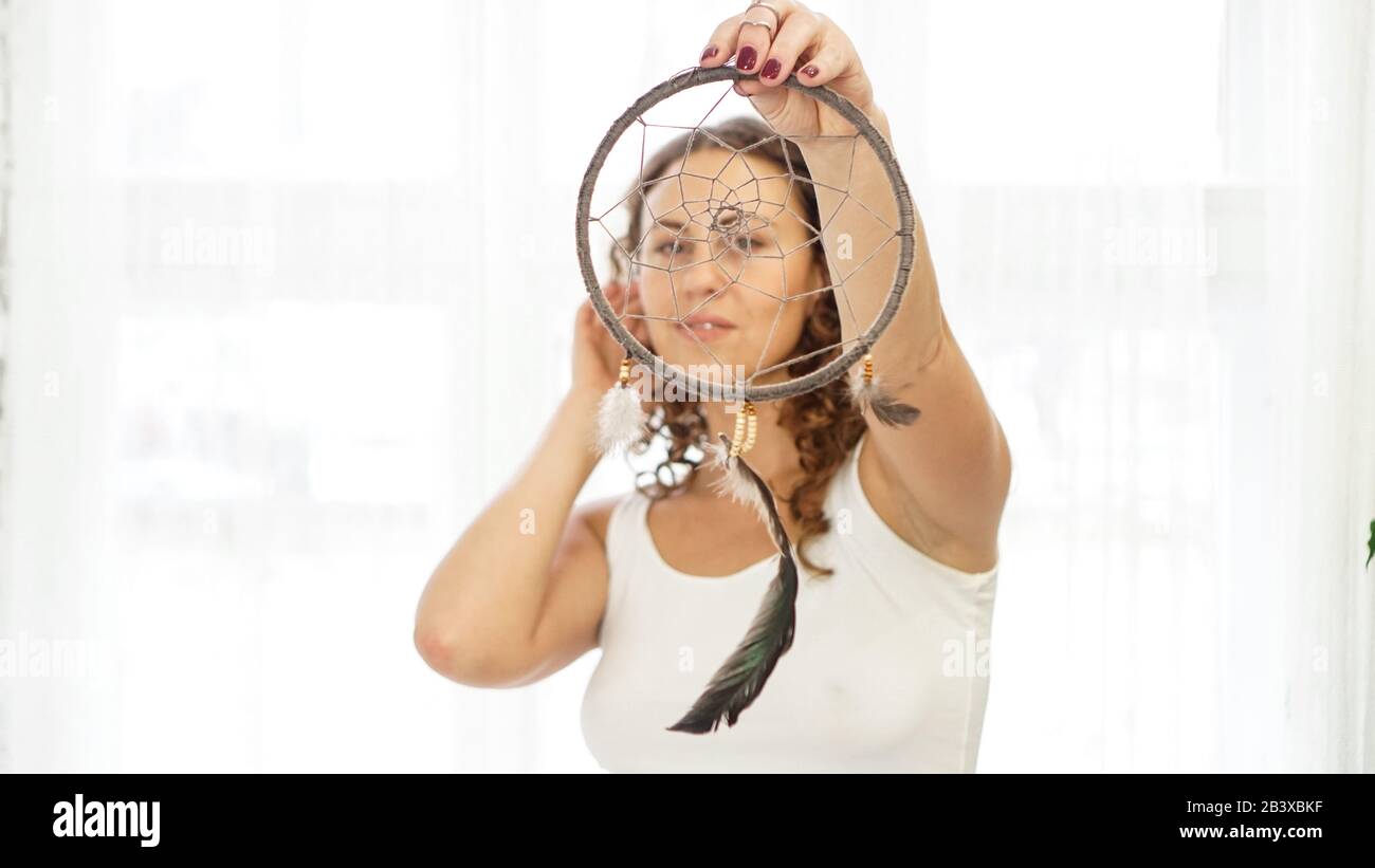Woman with curly hair with a dream catcher in hand in front of face ...