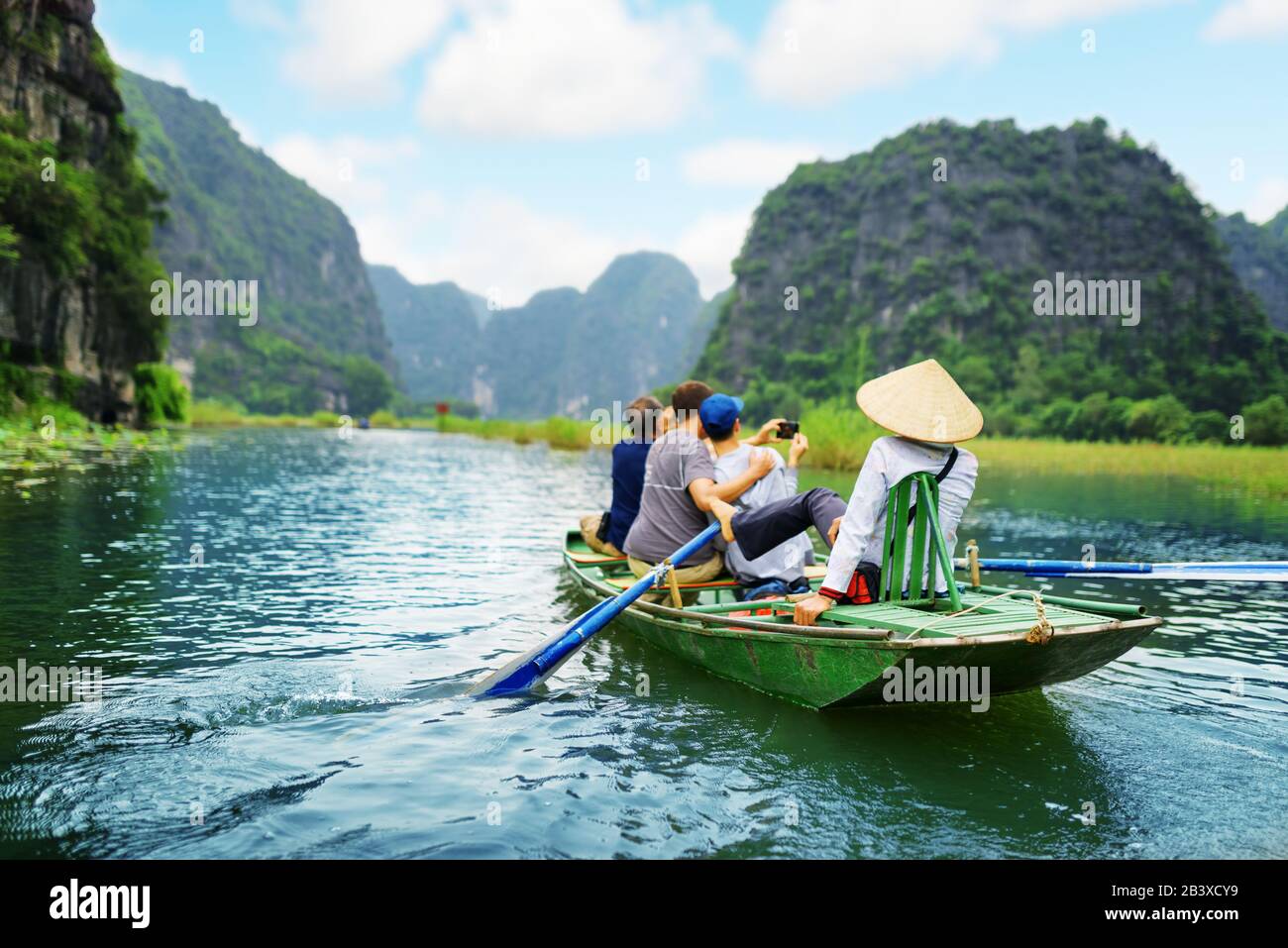 Tourists traveling in boat along the Ngo Dong River and taking picture of the Tam Coc, Ninh Binh, Vietnam. Rower using her feet to propel oars. Landsc Stock Photo