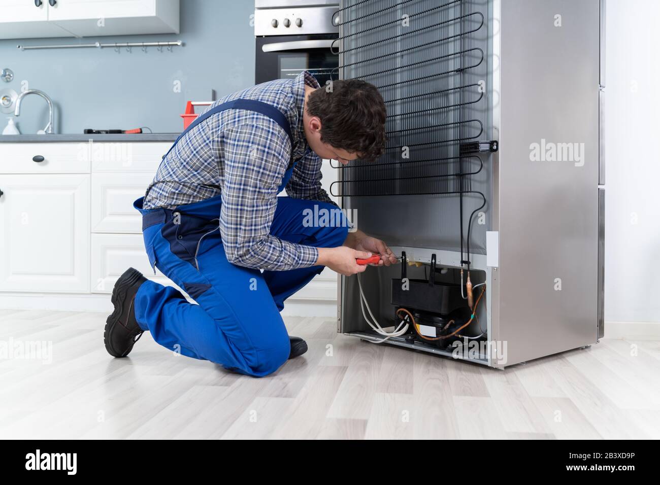 Male Worker Repairing Refrigerator With Screwdriver In House Stock Photo