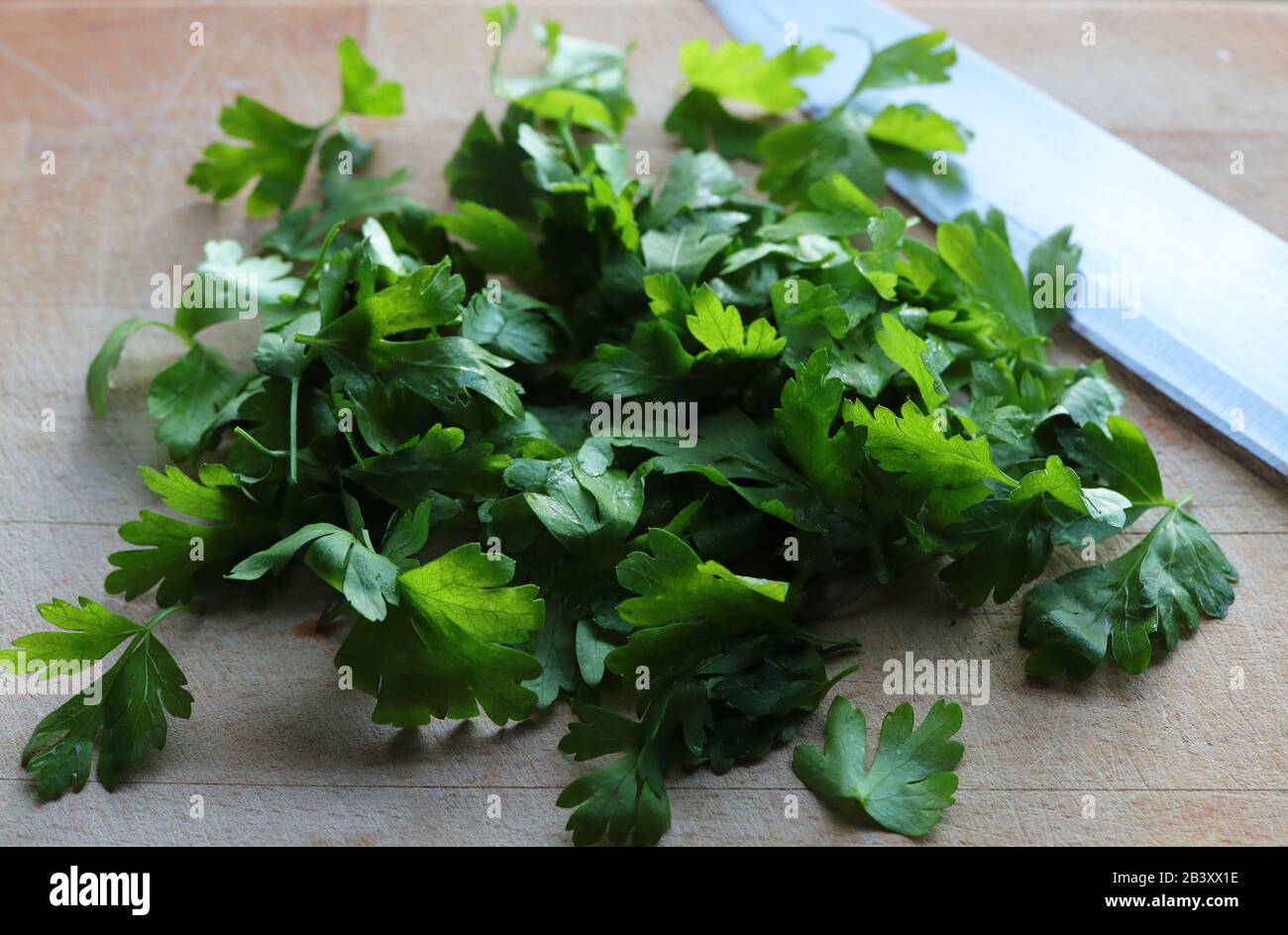 Parsley leaves on wood chopping board with large knife Stock Photo