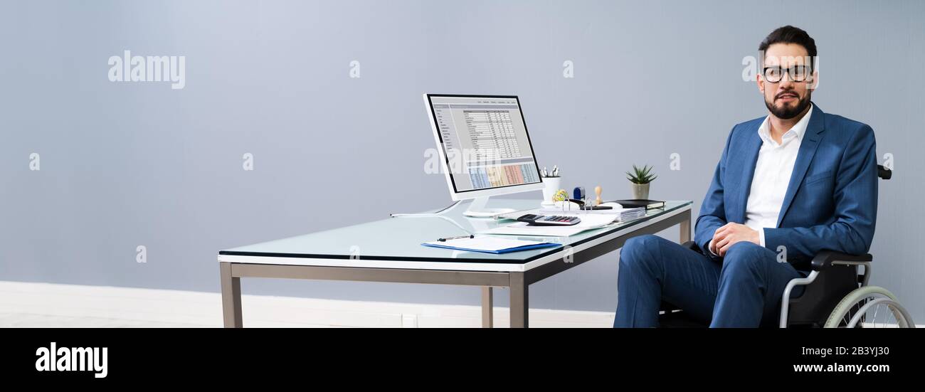 Happy Disabled Businessman On Wheelchair Near Computer Desk In Office