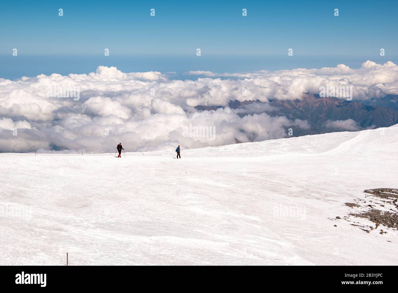 Landscape view of snow-capped hillside Mount Elbrus, Caucasus, Russia. A path leading down from the top. Two alpinists descending from the top. Clouds Stock Photo