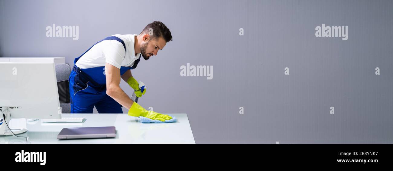 Worker Cleaning Computer Desk With Spray And Sponge Stock Photo