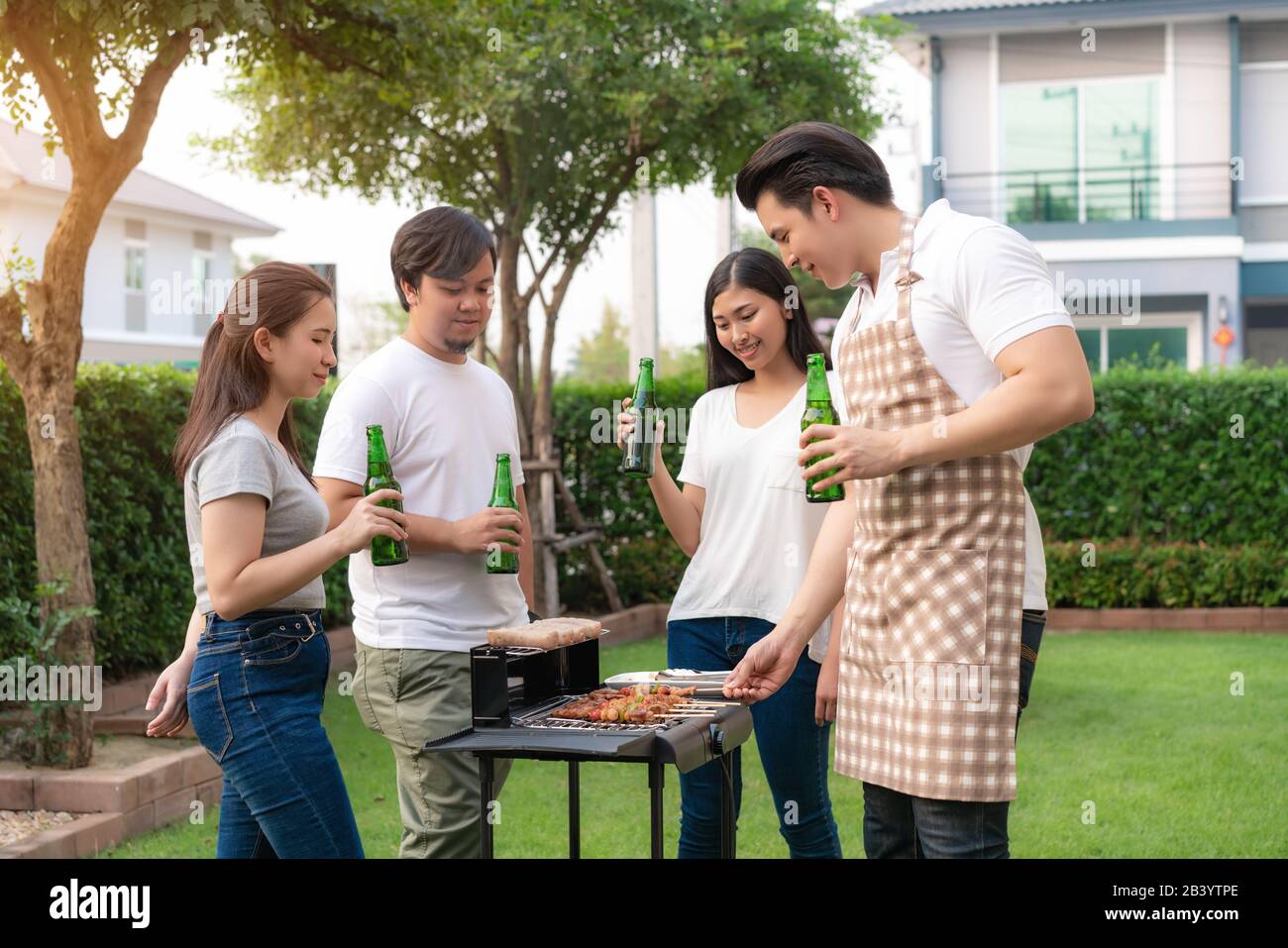 Asian man cooking barbeque grill and sausage for a group of friends to eat party in garden at home. group of friends having outdoor garden barbecue la Stock Photo