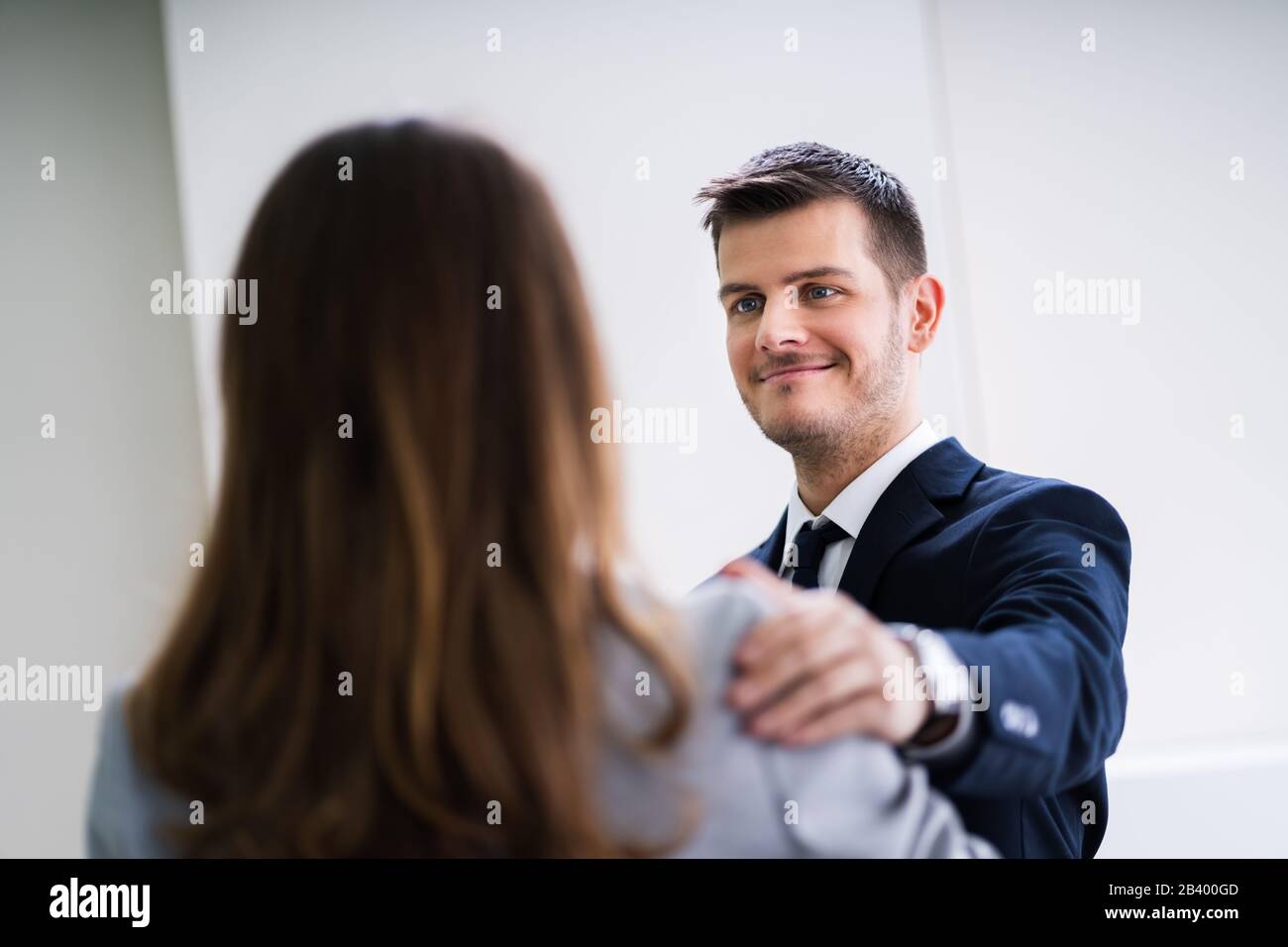 Businessman Putting His Hand On Female Colleague's Shoulder Congratulating Her On Success In Office Stock Photo