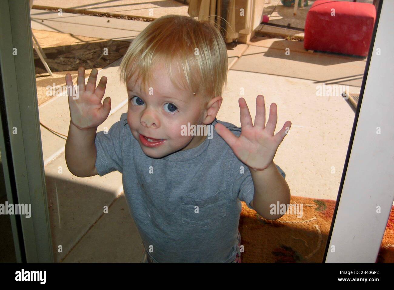 A little boy smushes his face into a sliding glass door. Stock Photo
