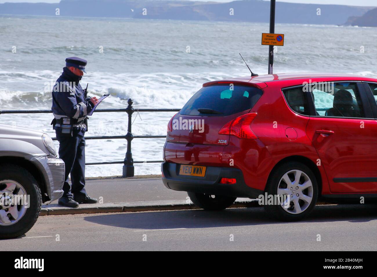 A traffic warden prepares a ticket for an illegally parked car. Stock Photo