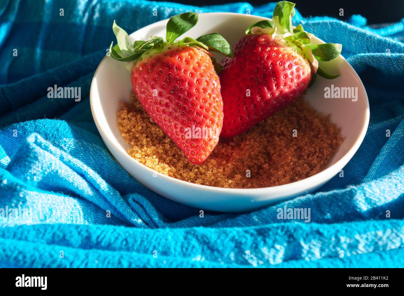 strawberries and cane sugar on blue cloth background, with natural light Stock Photo