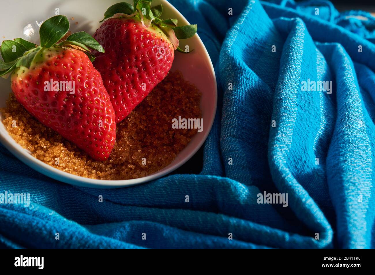 strawberries and cane sugar on blue cloth background, with natural ...