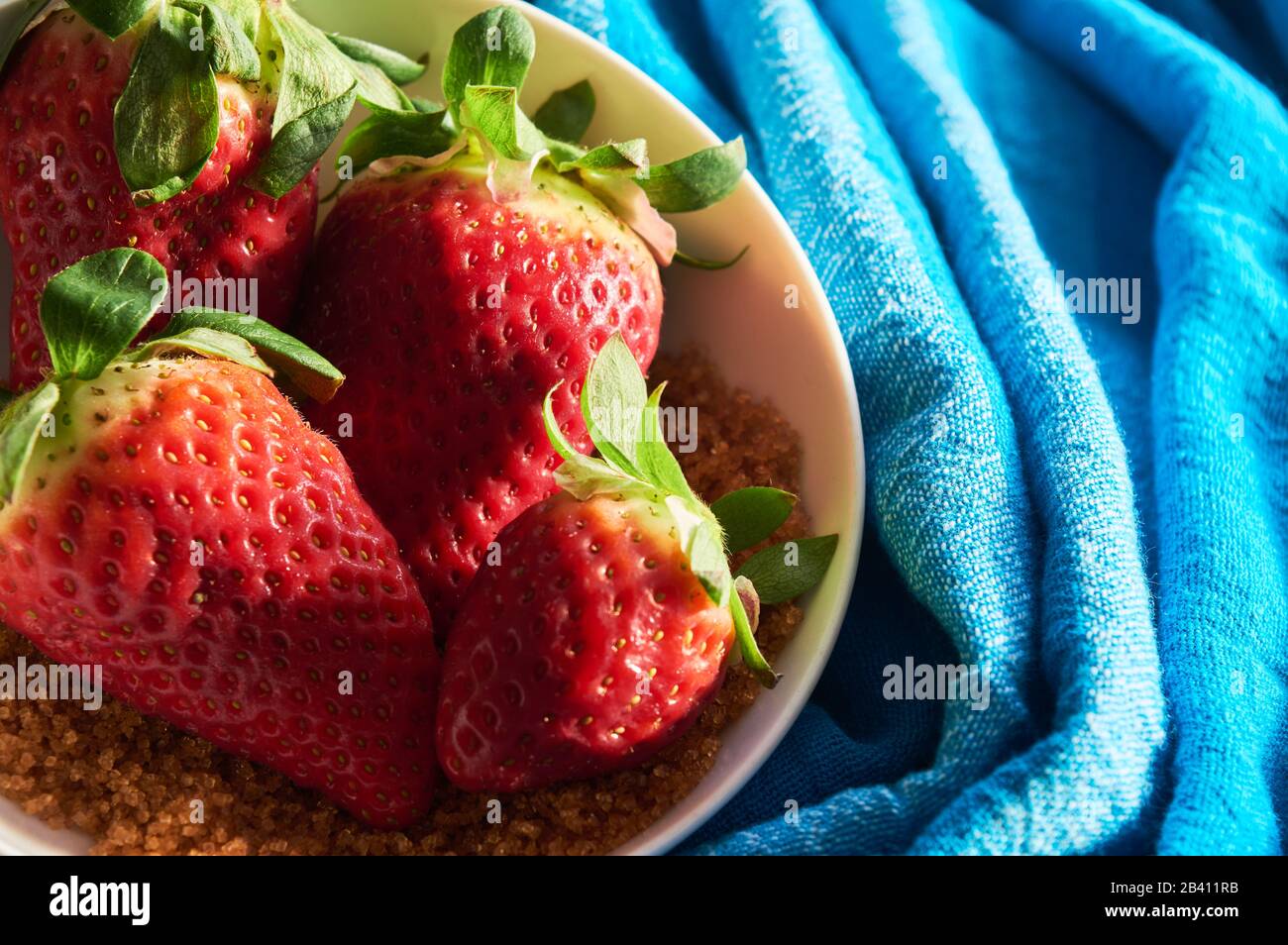 strawberries and cane sugar on blue cloth background, with natural ...