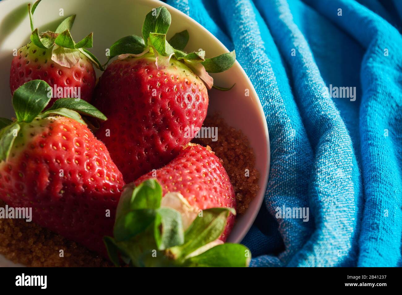 strawberries and cane sugar on blue cloth background, with natural ...