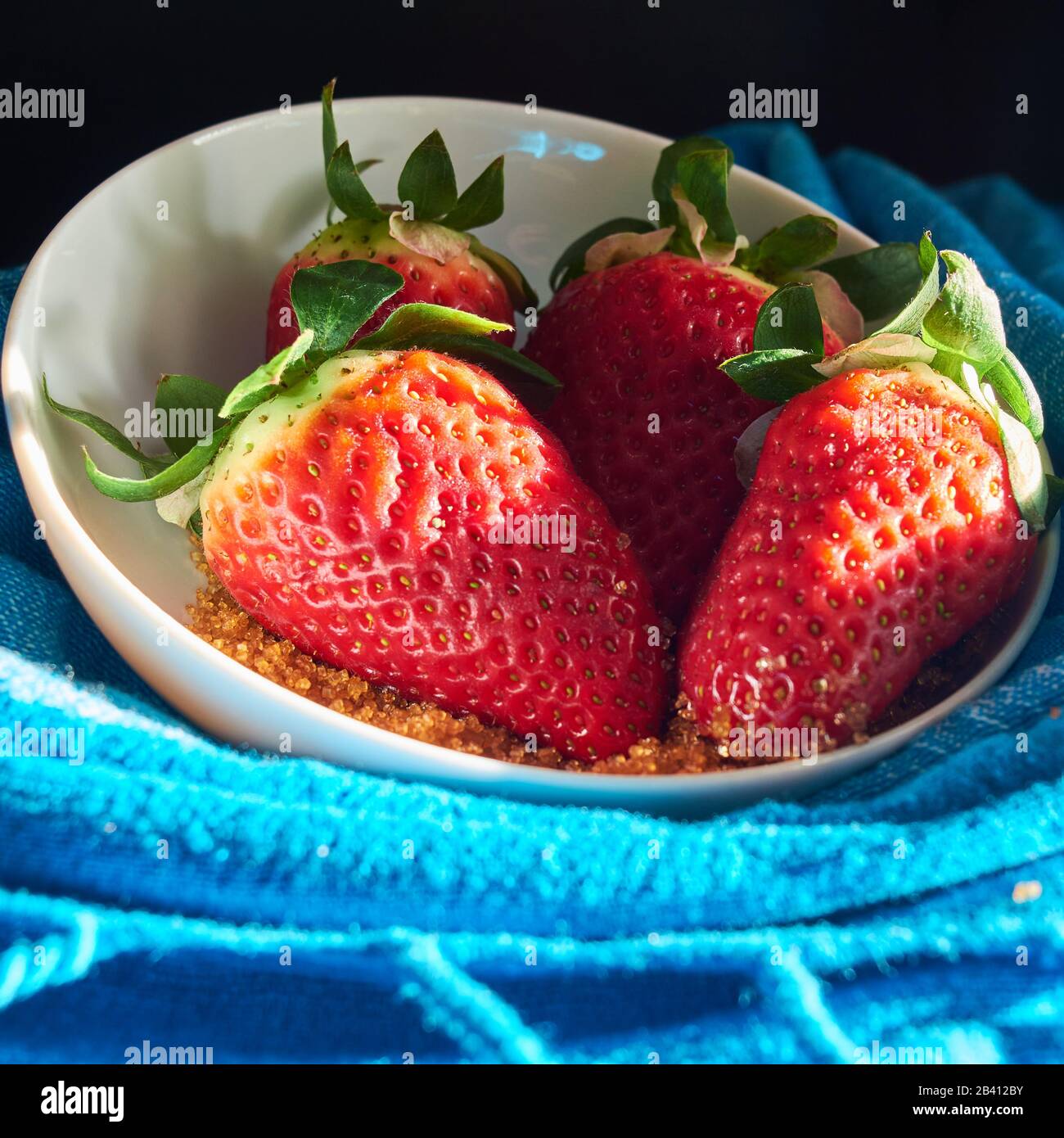 strawberries and cane sugar on blue cloth background, with natural ...