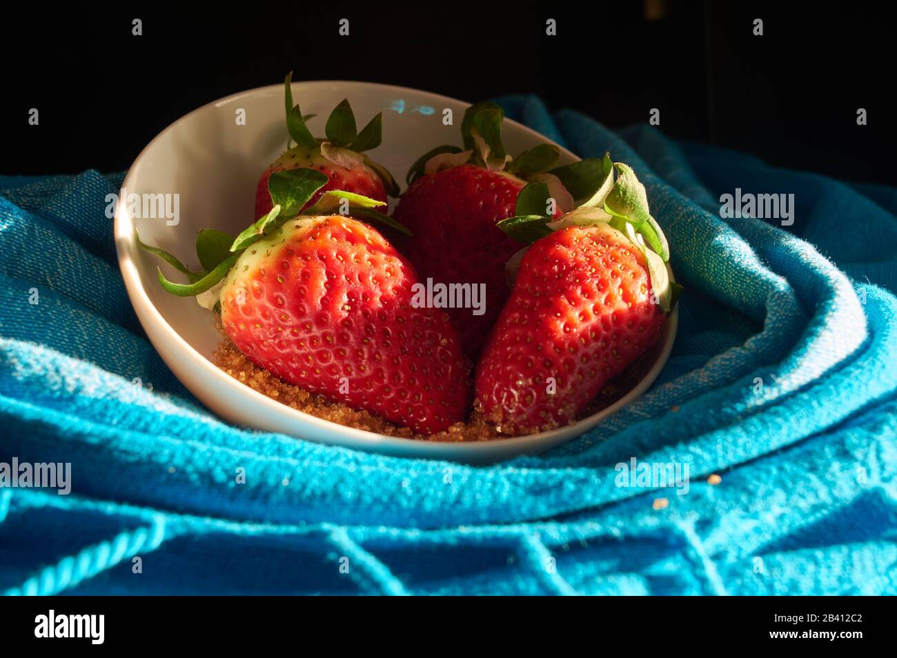 strawberries and cane sugar on blue cloth background, with natural ...
