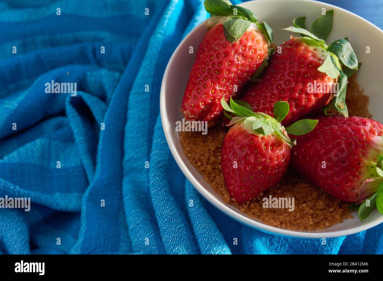 strawberries and cane sugar on blue cloth background, with natural ...