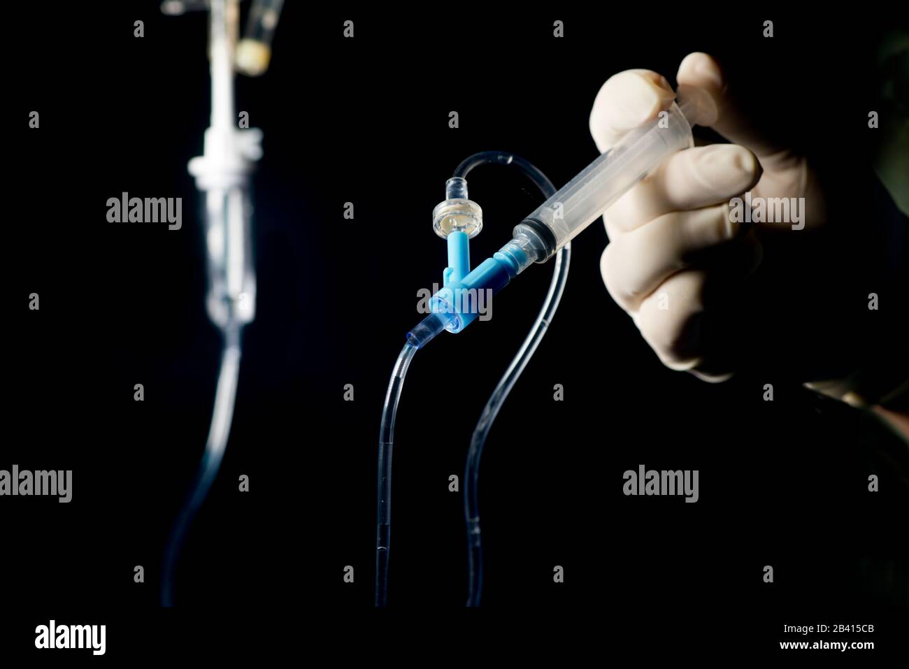 Nurse pushes IV medication by syringe into IV medication port with dark background. Stock Photo