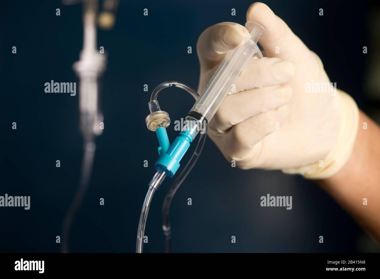 Nurse pushes IV medication by syringe into IV medication port with blue background. Stock Photo