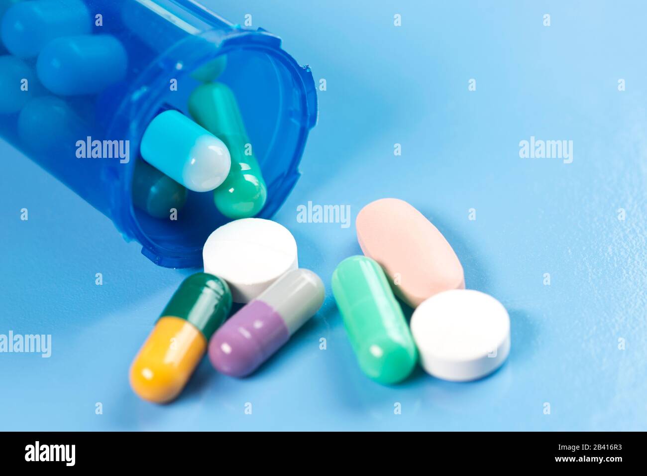 Colorful capsule and tablets spill from blue prescription container on blue background. Stock Photo