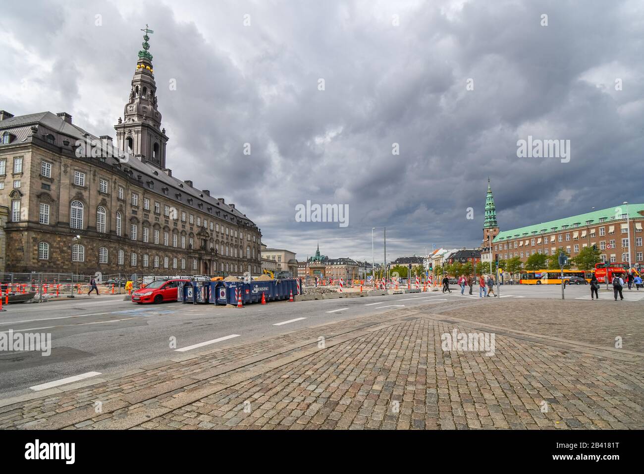 Tourists and Danes walk past construction work in the Hojbro Plads main square with the spire of St Nicholas church and Christiansborg Slot in view Stock Photo