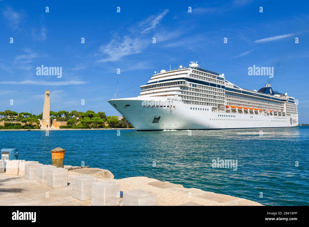 A massive cruise ship pulls near the Sailors Monument in the cruise port and harbor at Brindisi, Italy, in the Southern Puglia region. Stock Photo