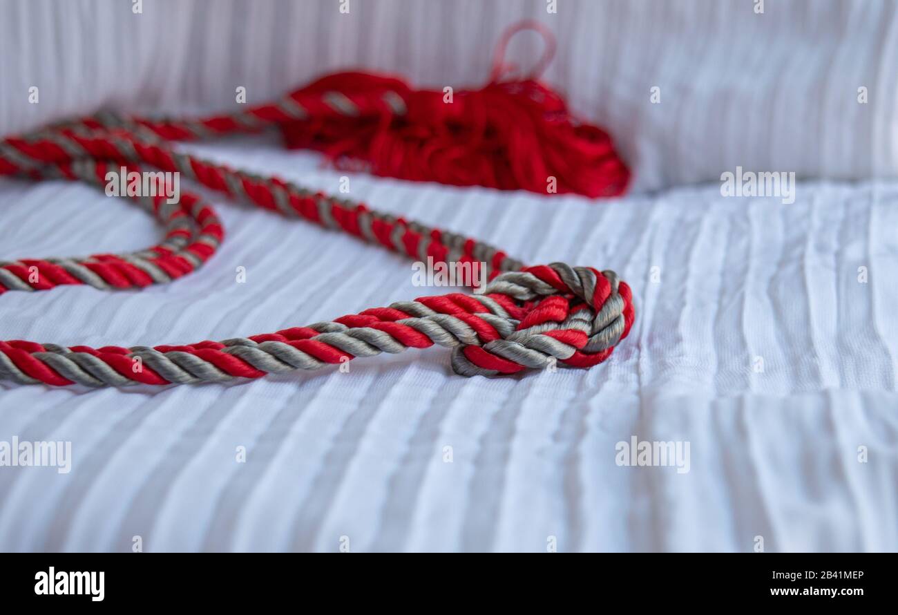 A pretty silver and red cord knotted together and displayed on a white textured background with bokeh effect and copy space. Stock Photo