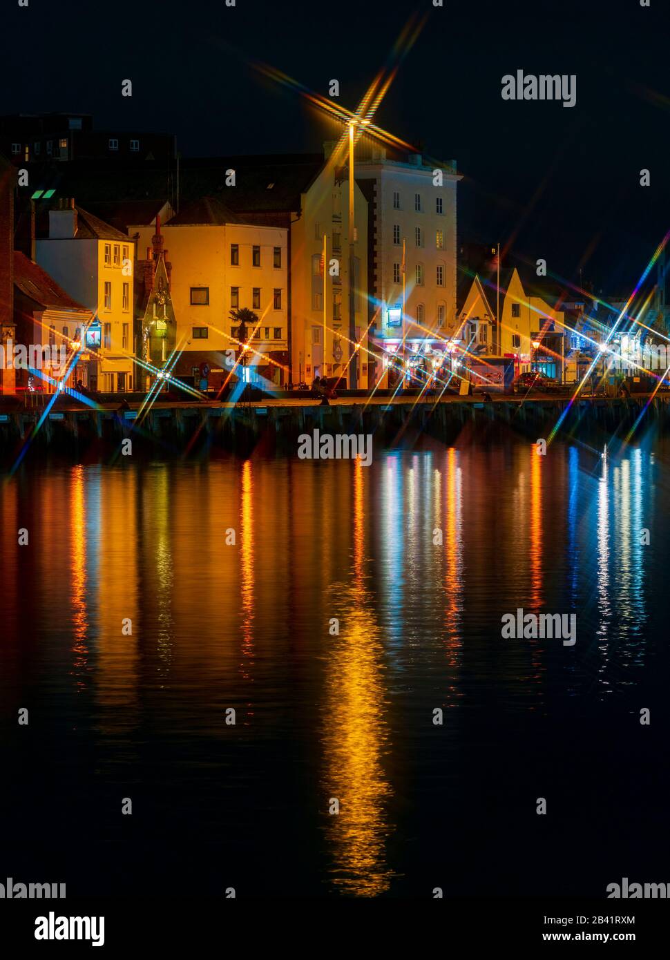 Bright street lights cast star shapes and reflections in the still waters of Poole Quay Stock