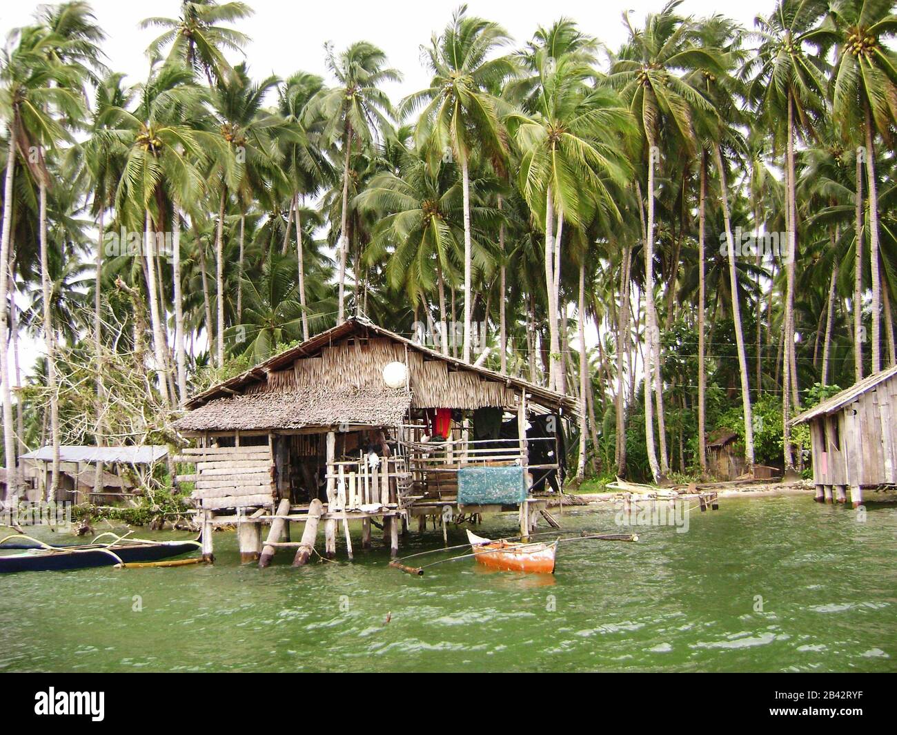 Medium wide shot of a house on stilts with boats in front in a fishing village in Surigao del Sur, Philippines Stock Photo