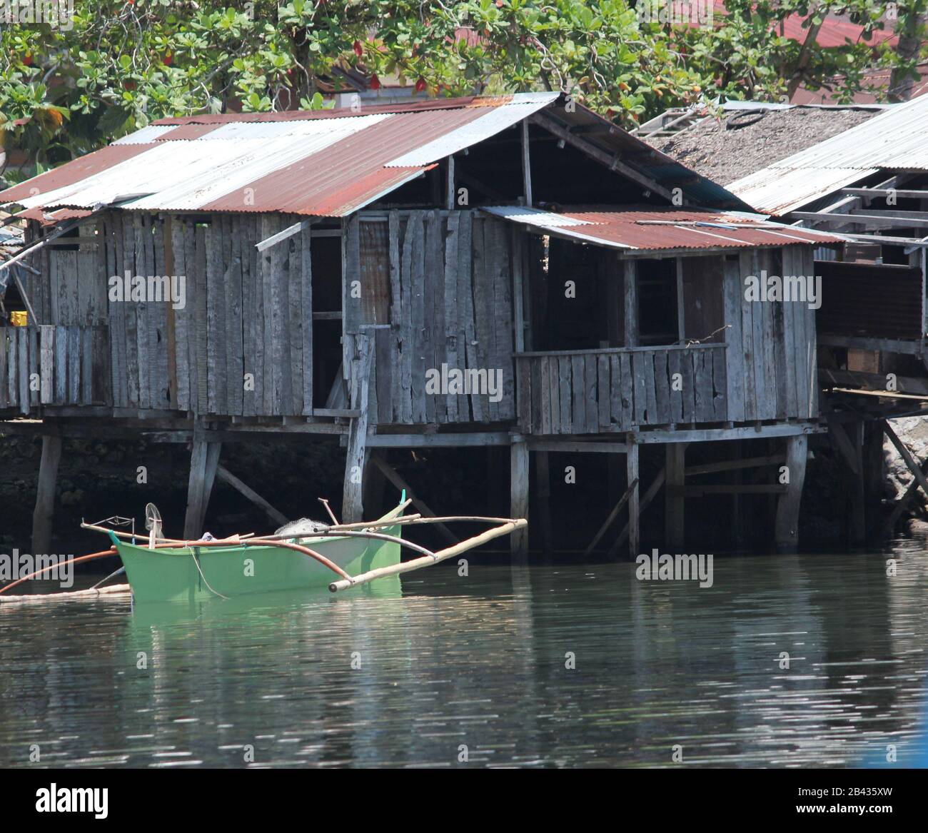 Coconut log house on stilts with an outrigger boat in the water. Stock Photo