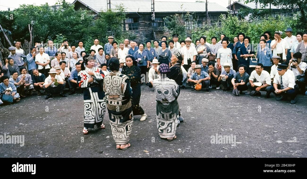 Five Ainu women in traditional dress dance for Japanese tourists visiting their village on the island of Hokkaido in northern Japan. There were only 300 pure-blooded Ainu (pronounced I-noo) still living when this historical photograph was taken in 1962. Since that time the Ainu have assimilated into Japanese society and their age-old crafts, customs and ceremonies are only kept alive in special villages for tourists. The Ainu were officially recognized as indigenous people of Japan in 2008. Stock Photo
