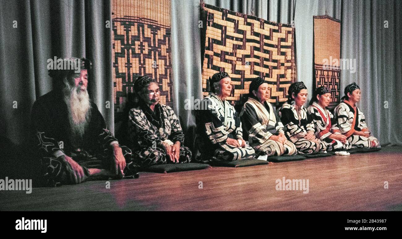 An old bearded chief and six elderly Ainu women rest before performing traditional Ainu dances, chants and hand-clapping to entertain Japanese tourists on the island of Hokkaido in northern Japan. Only 300 pure-blooded Ainu (pronounced I-noo) were still living when this historical photograph was taken in 1962. Since that time the Ainu have assimilated into Japanese society and their age-old way of life is only glimpsed today in special tourist villages. The Ainu were officially recognized as indigenous people of Japan in 2008. Stock Photo