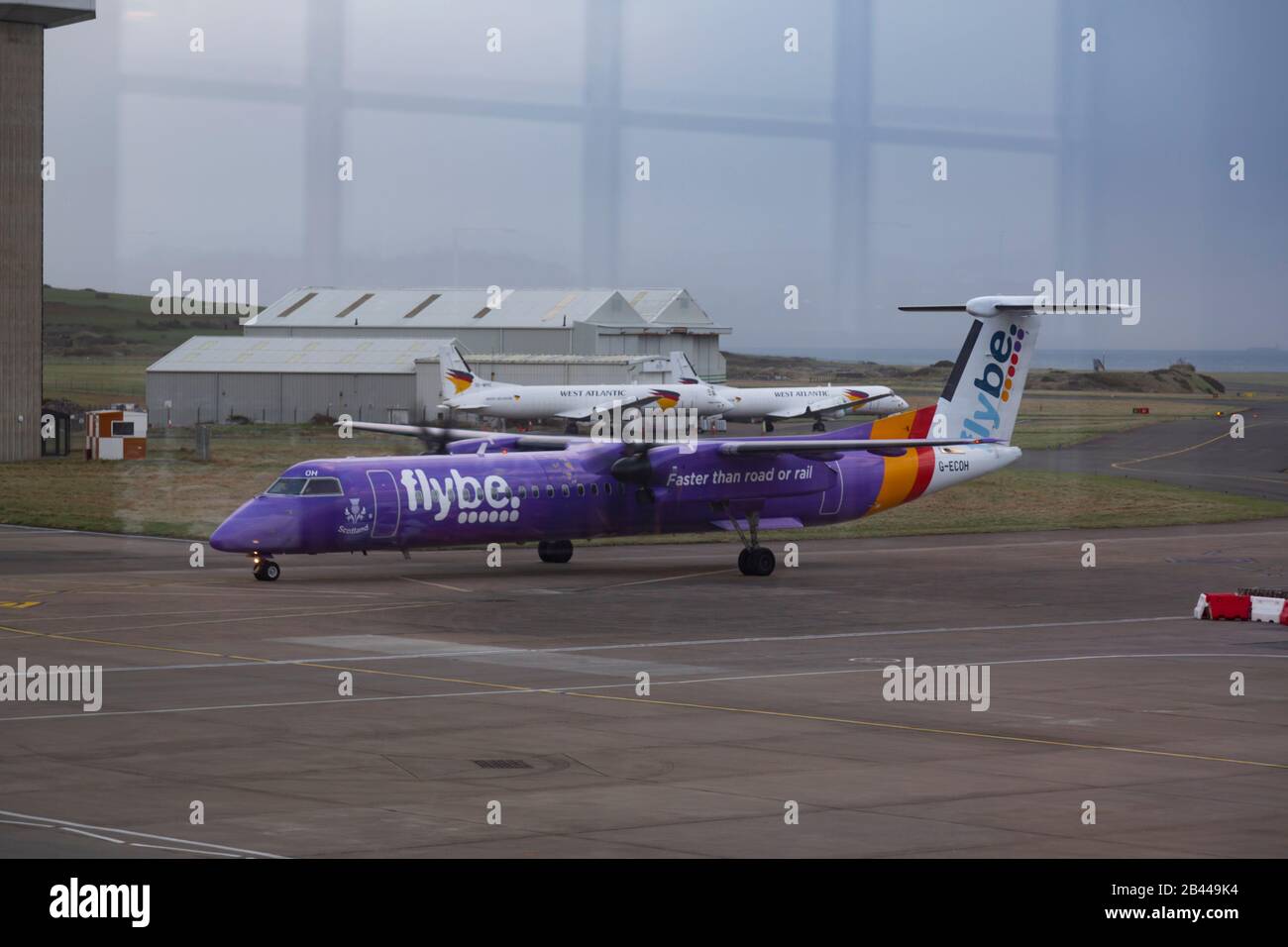 4 February 2020: FlyBe plane arriving at Isle of Man Airport seen through the departure lounge window. The airline company, Flybe,entered Administration (collapsed) on 5 March 2020. All flights have been grounded and the UK business has ceased trading with immediate effect. The collapse was partially blamed on COVID-19 making FlyBe is the Uk's 'first corporate coronavirus victim'. Patches of faking paint can be clearly seen on the body of the plane. Customers are advised to monitor the Civil Aviation Authority website. Stock Photo