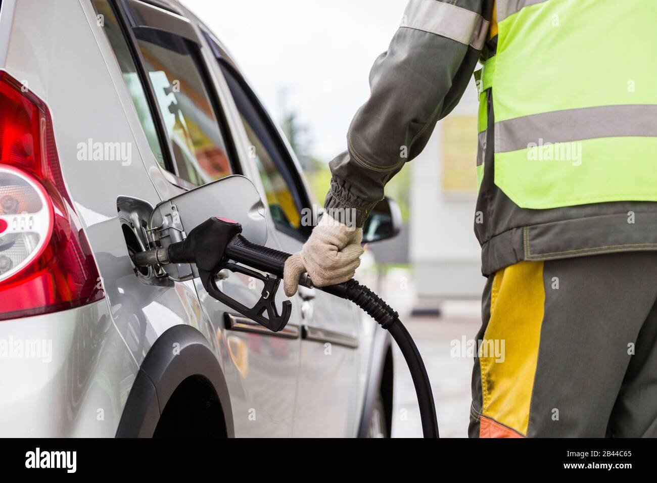 hand in white cotton fabric glove refueling gray metallic car on gas