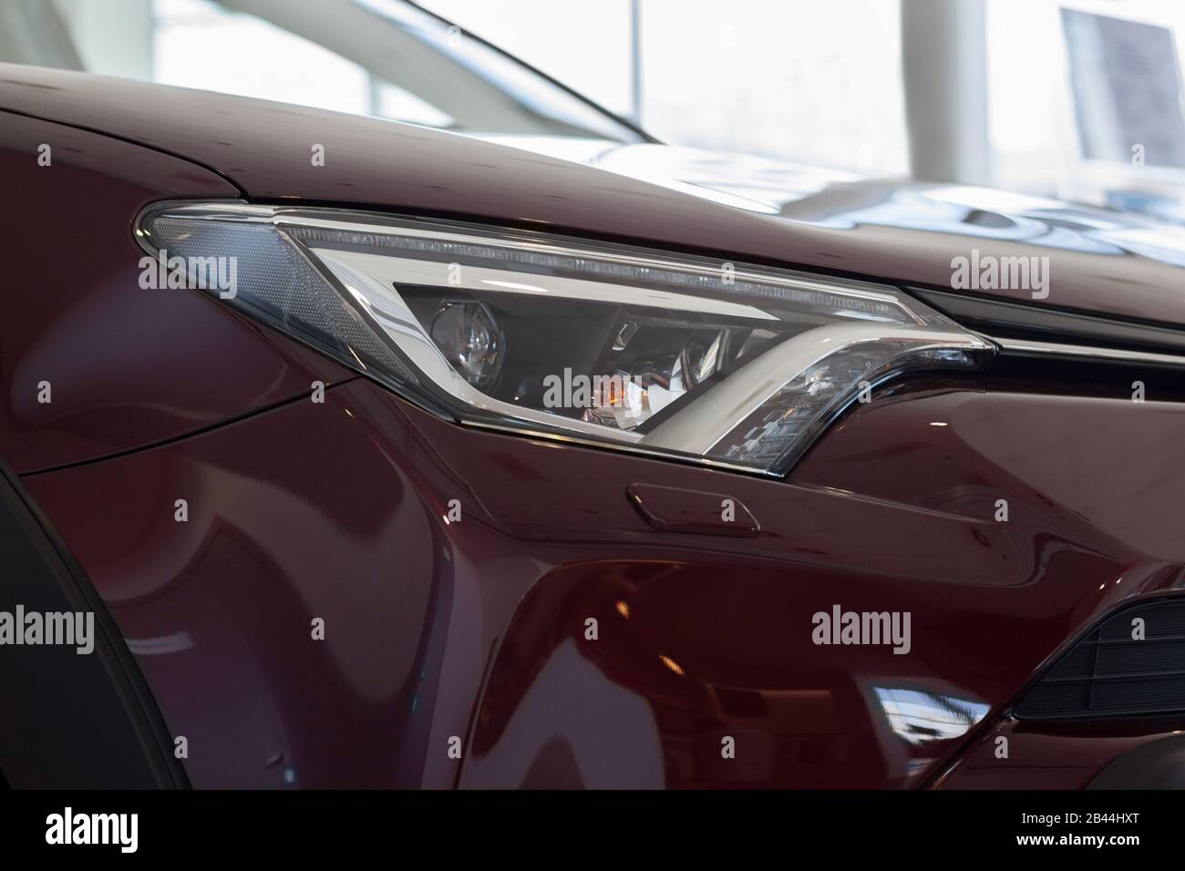 New vehicle of cherry color with elegant head lamps in showroom. Side view. Stock Photo