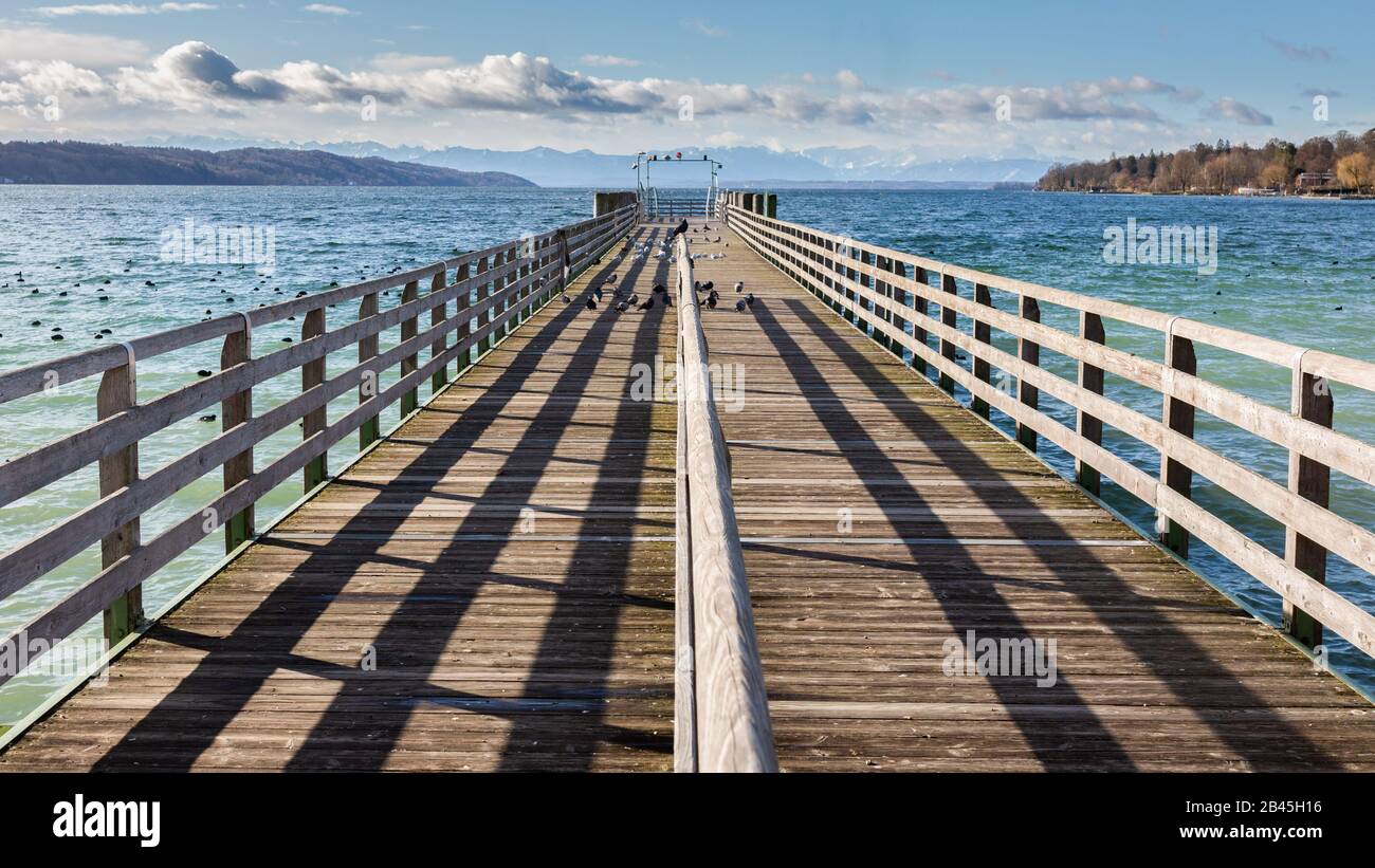 Straight view on a wooden pier at Lake Starnberg (Starnberger See). Alps in the distance. Concept for chance, new beginning, opportunities, start. Stock Photo