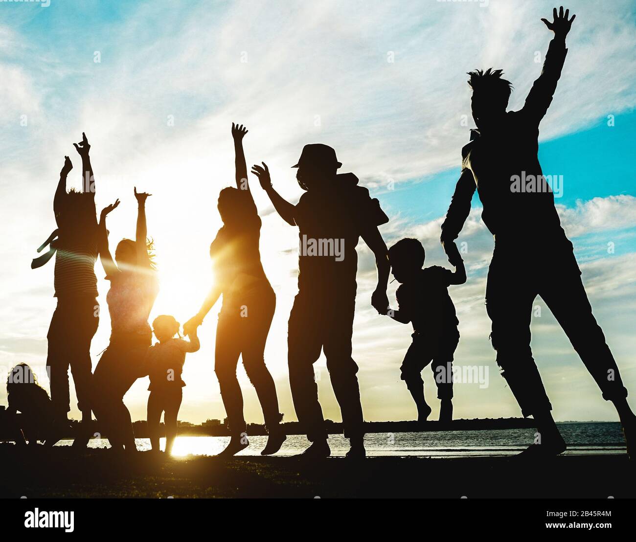 Silhouette of big family having fun on the beach at sunset - Father, mother, children and uncles enjoying time together - Focus on bodies - Love, rela Stock Photo