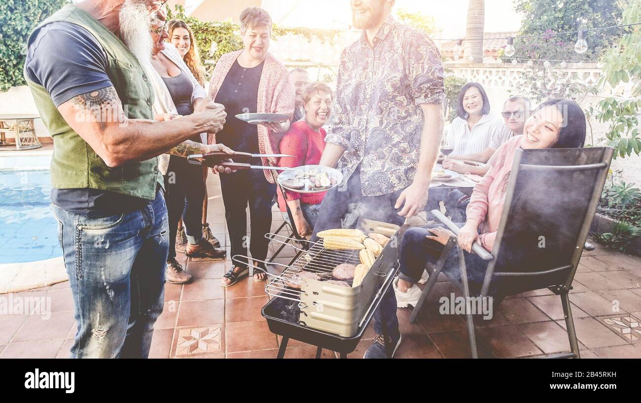 Father cooking and serving meat at barbecue dinner outdoor - Man grilling food for friends at bbq meal outside - Summer lifestyle, and family concept Stock Photo