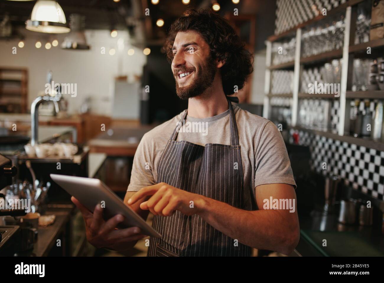 Portrait of successful young caucasian cafe owner standing behind counter using digital tablet Stock Photo