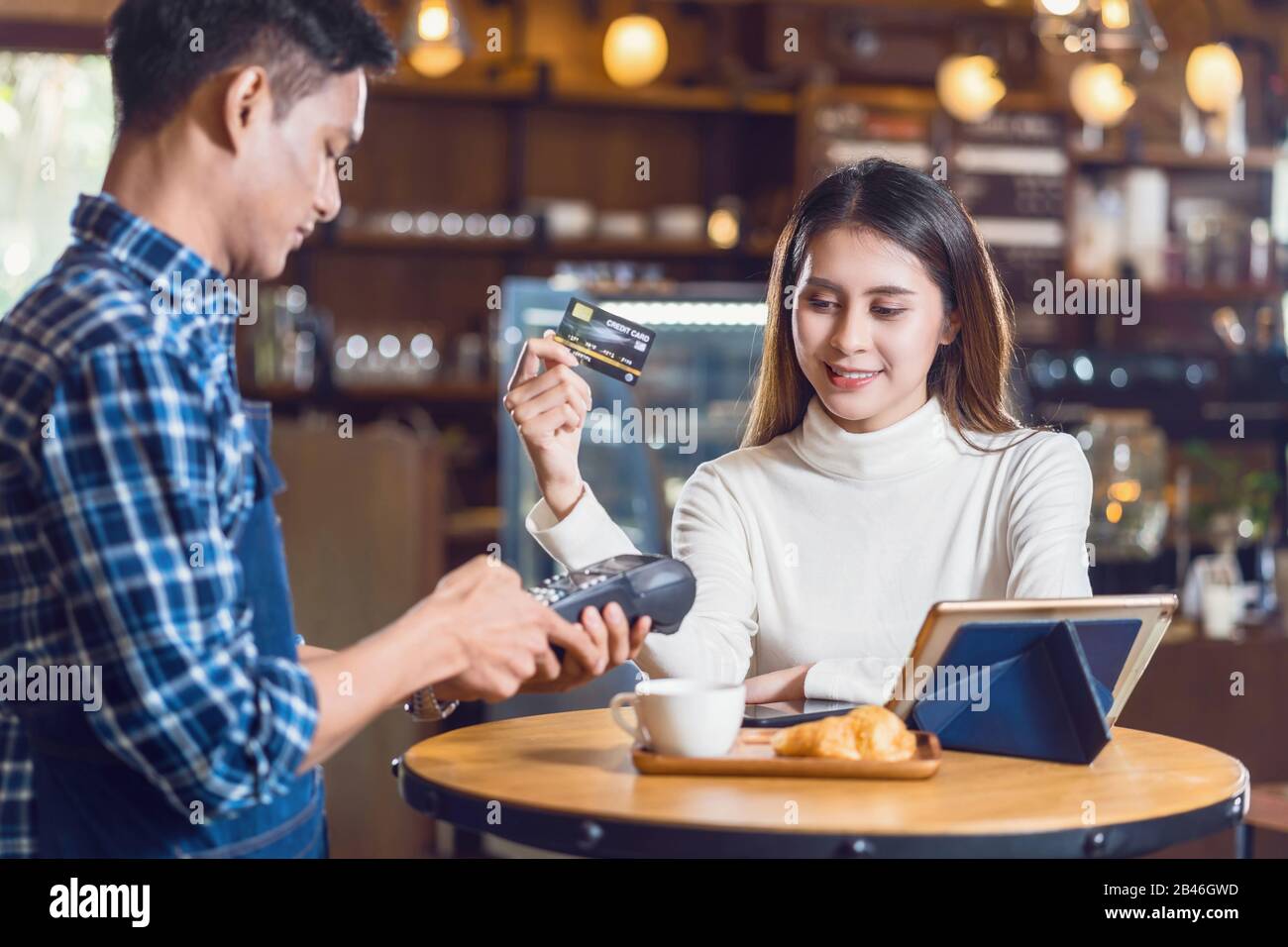 Asian customer woman paying with credit card via contactless nfs technology to Asian Small Coffee shop owner at the female table in cafe, Small busine Stock Photo