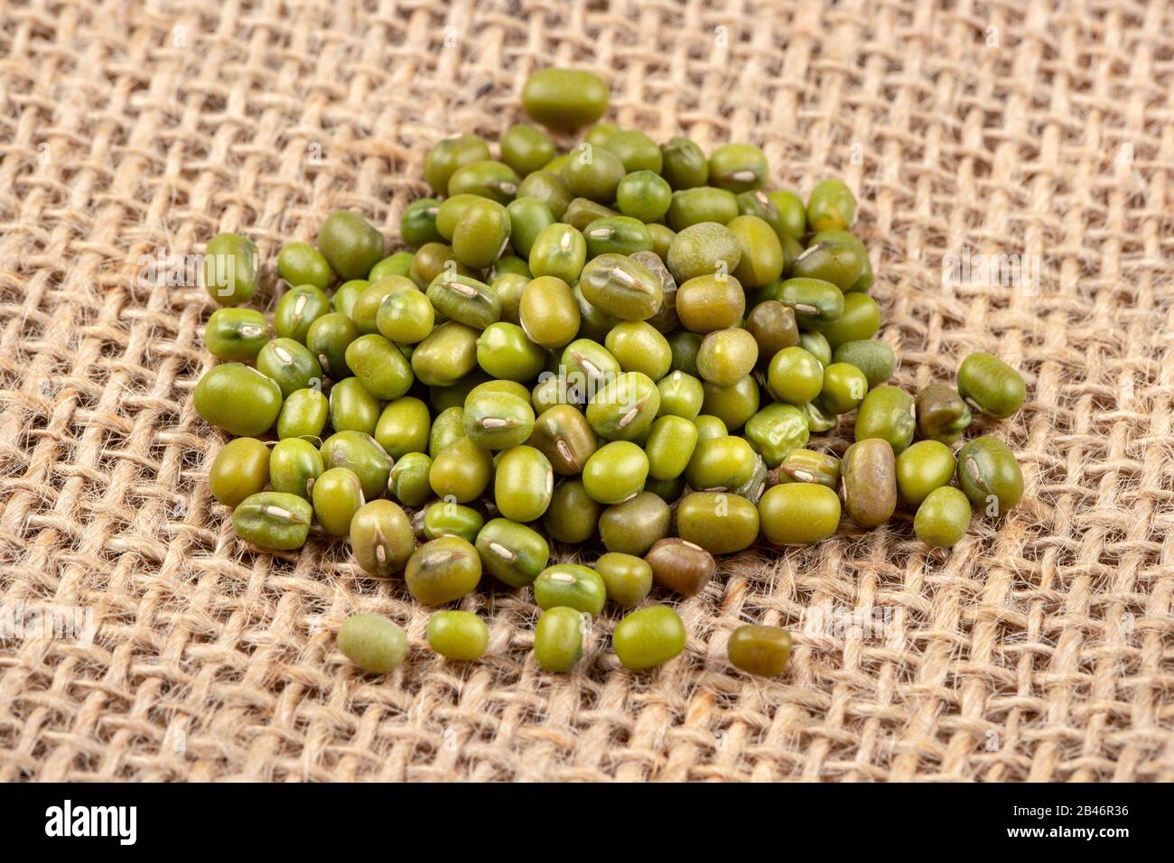Pile of raw green mung grains scattered on burlap Stock Photo