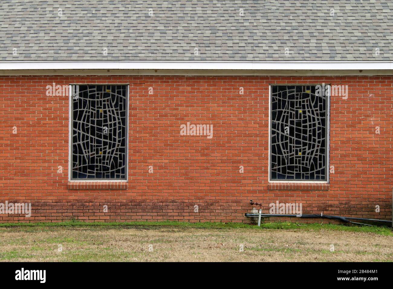 a pair of stained glass church windows on a red brick wall Stock Photo