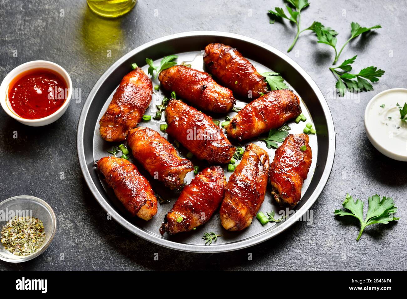 Bacon wrapped grilled chicken wings on plate over dark stone background