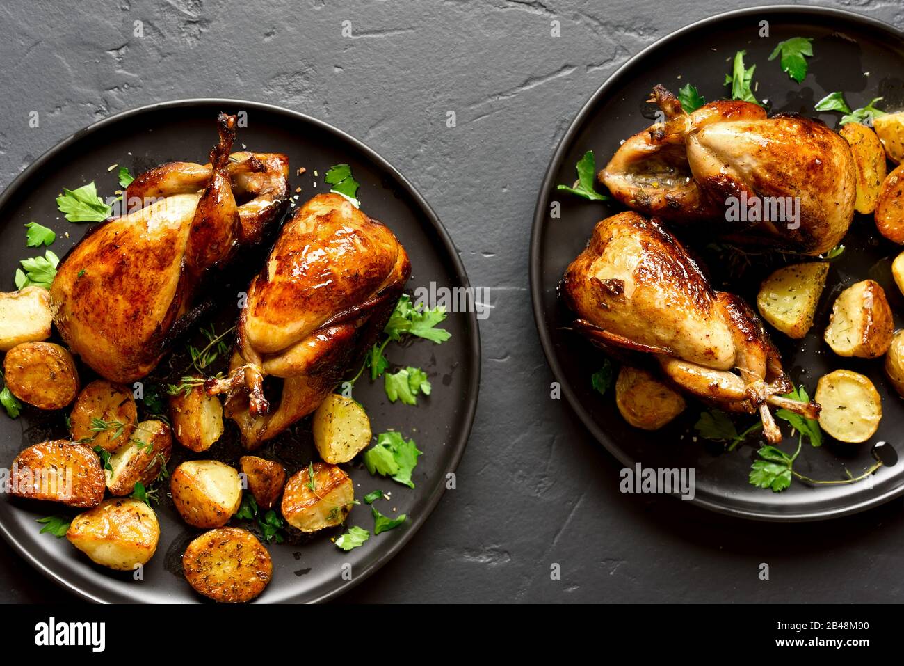 Tasty grilled quails with baked potato wedges on black stone background ...