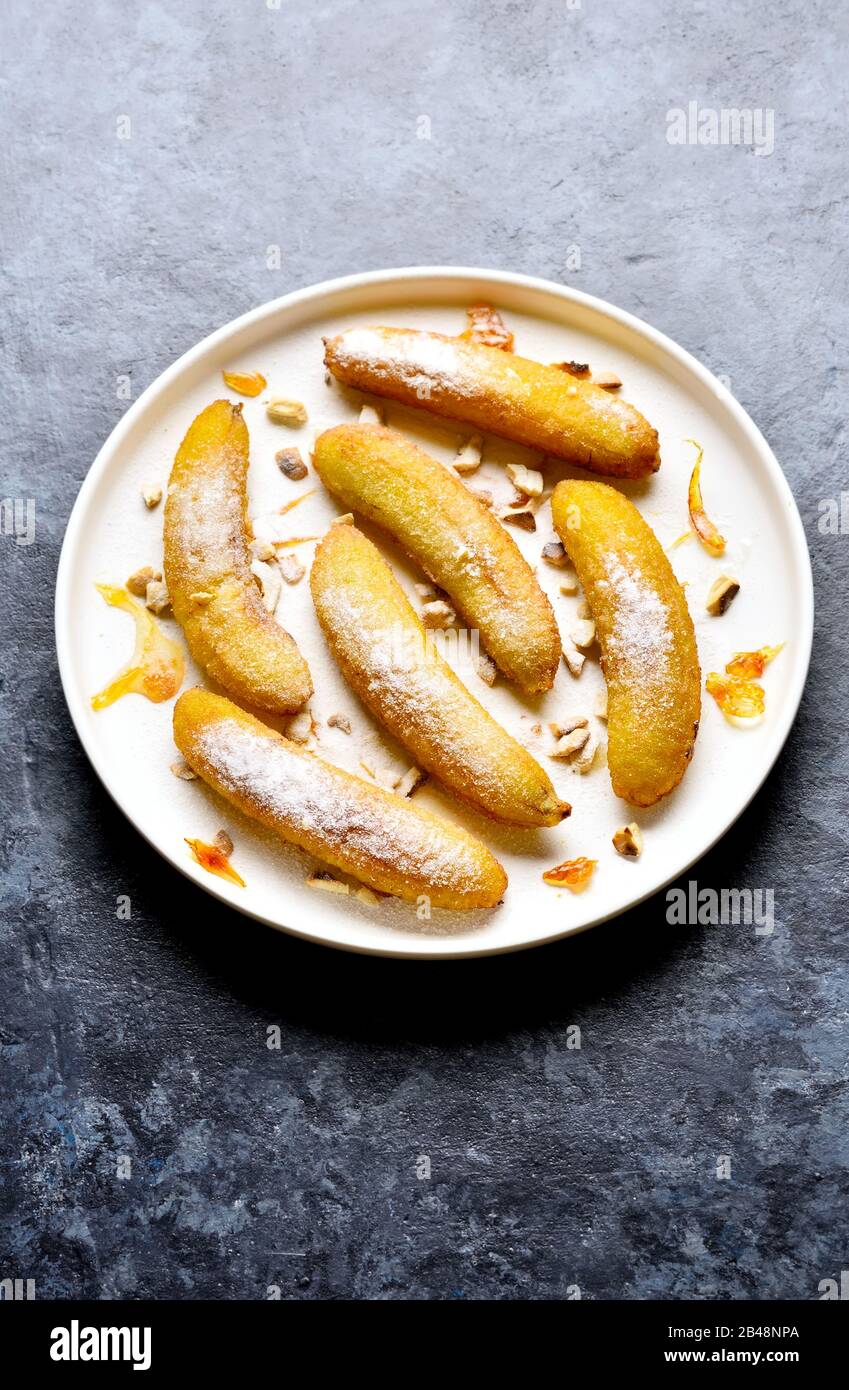 Deep fried bananas on white plate over blue stone background with free