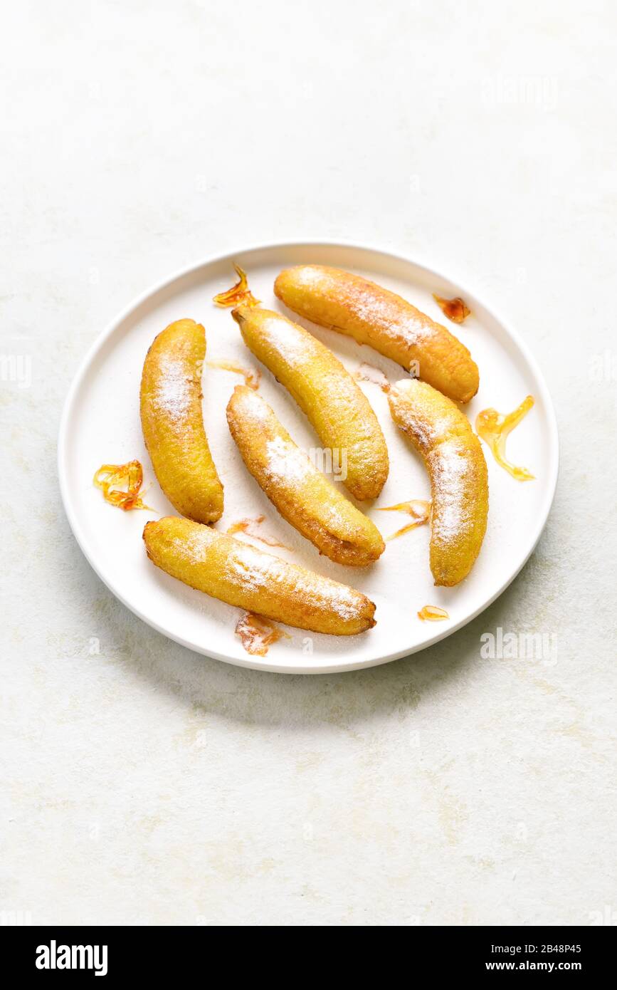 Deep fried bananas on plate over light stone background with free space