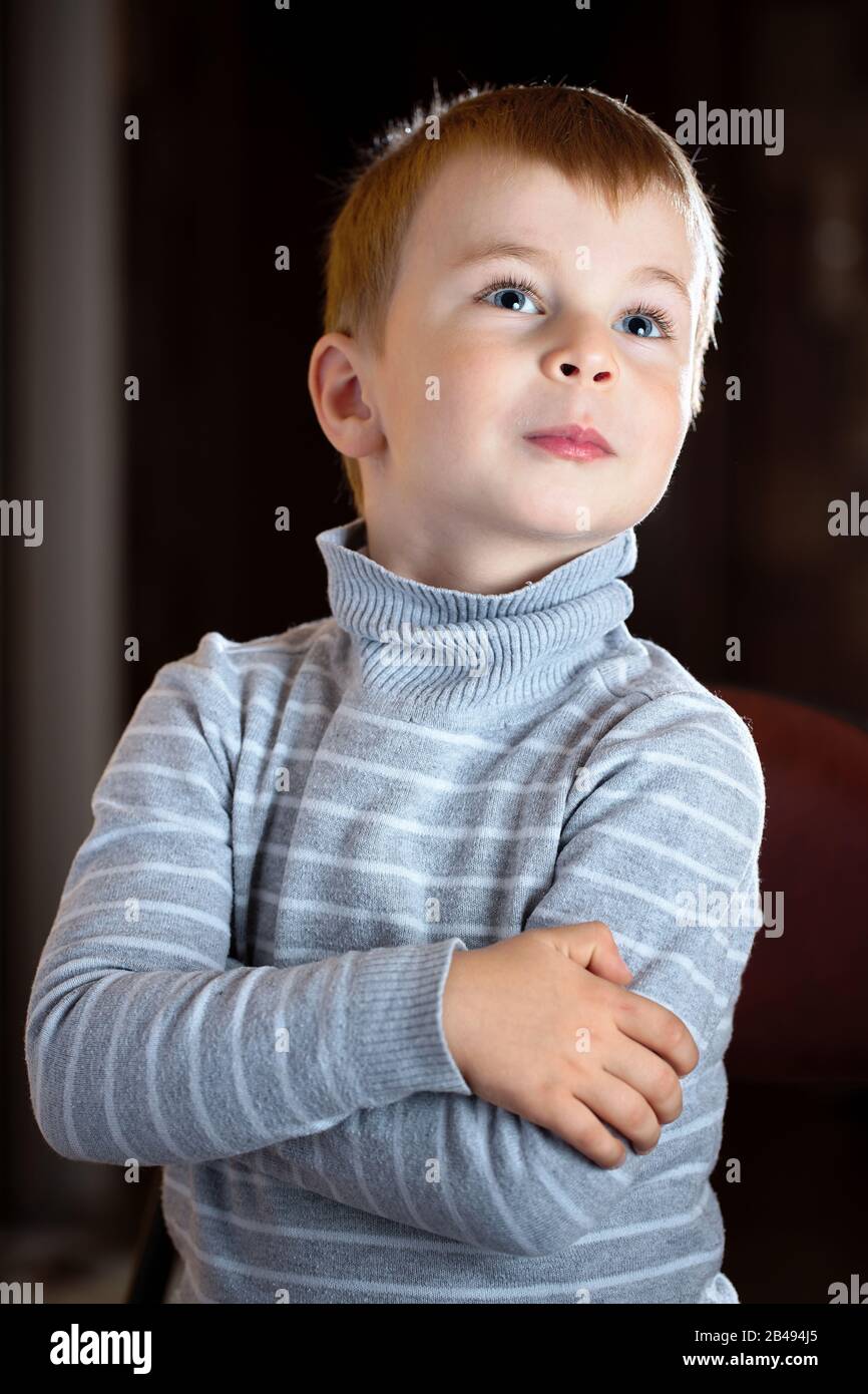 Facial portrait of dreamy pensive blond boy with gaze his eyes fixed upwards over dark background, with specks of dust flying in backlight with flares Stock Photo