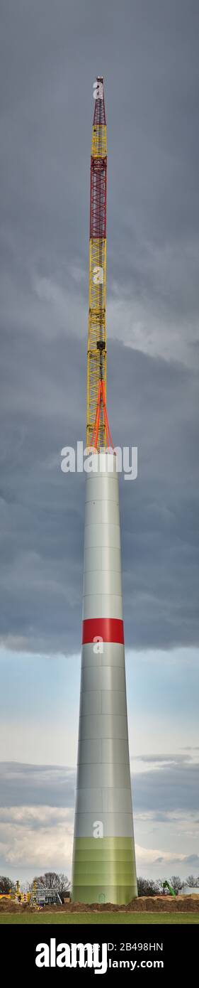 Construction of a wind turbine with an enormous crane, dramatic grey clouds in the background, stitched picture in high resolution Stock Photo