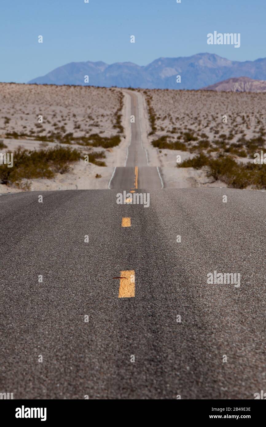 Straight long road winds through the desert to the horizon, with dotted orange dividing line on focus in the foreground Stock Photo